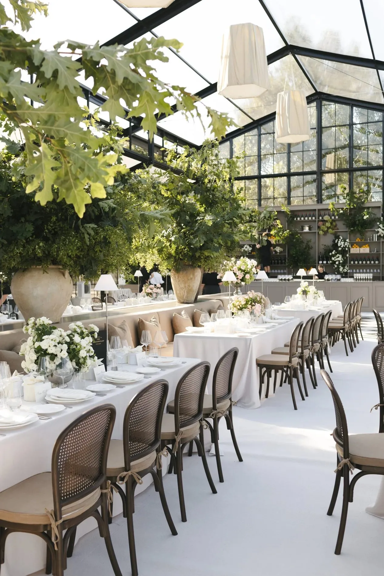 Clear-roof glasshouse marquee wedding reception with greenery and long banquet tables